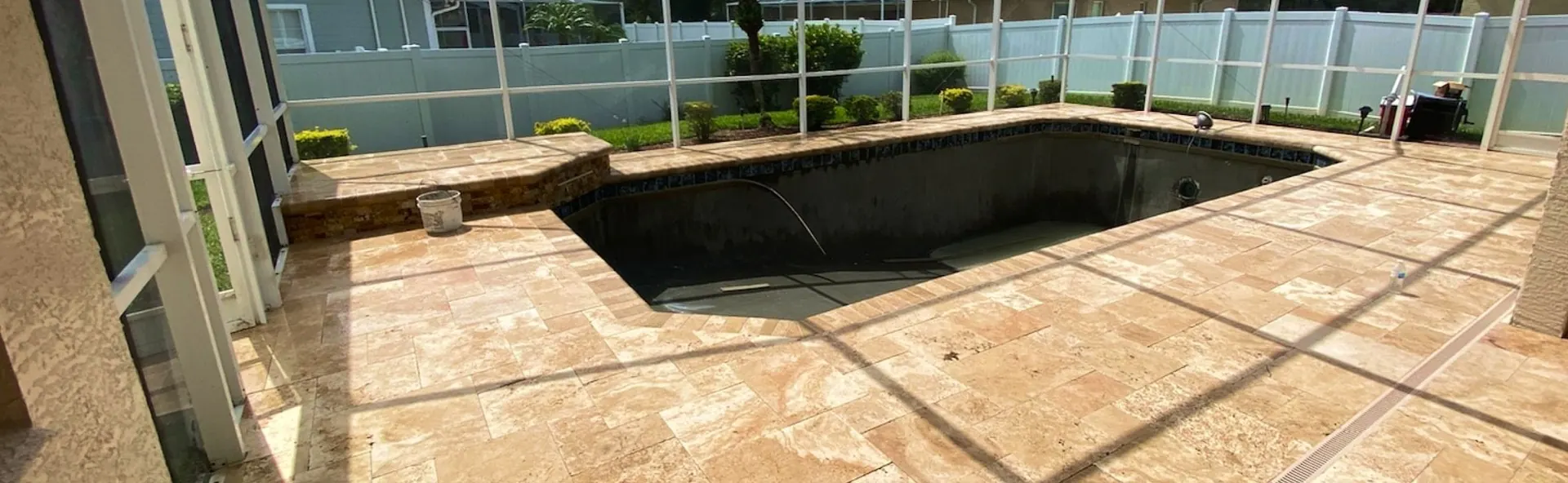 Paver pool deck inside a screen enclosure, lined with hedges